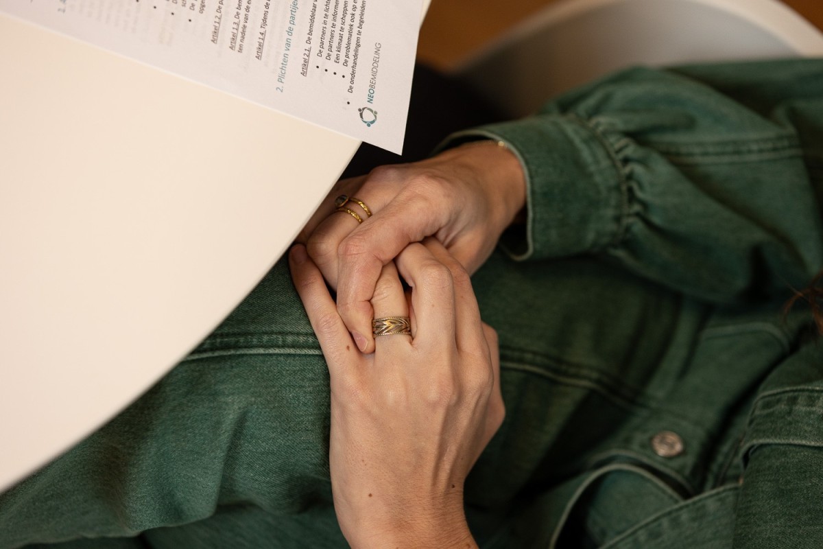 Een vrouw die in haar handen wrijft en haar trouwring aanraakt terwijl ze aan een tafel zit